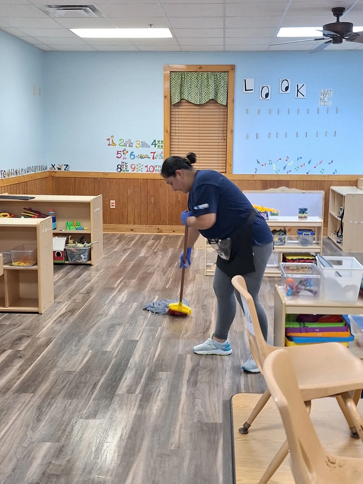 Rivera team member mopping a classroom floor beside shelves and chairs