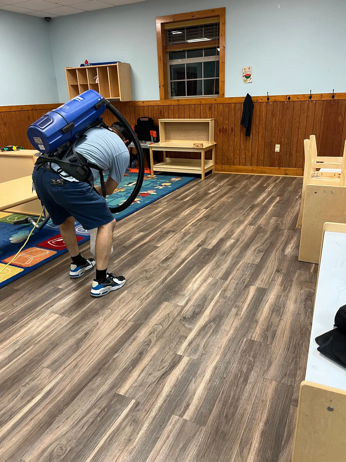 Rivera team member using a backpack vacuum to clean a classroom floor
